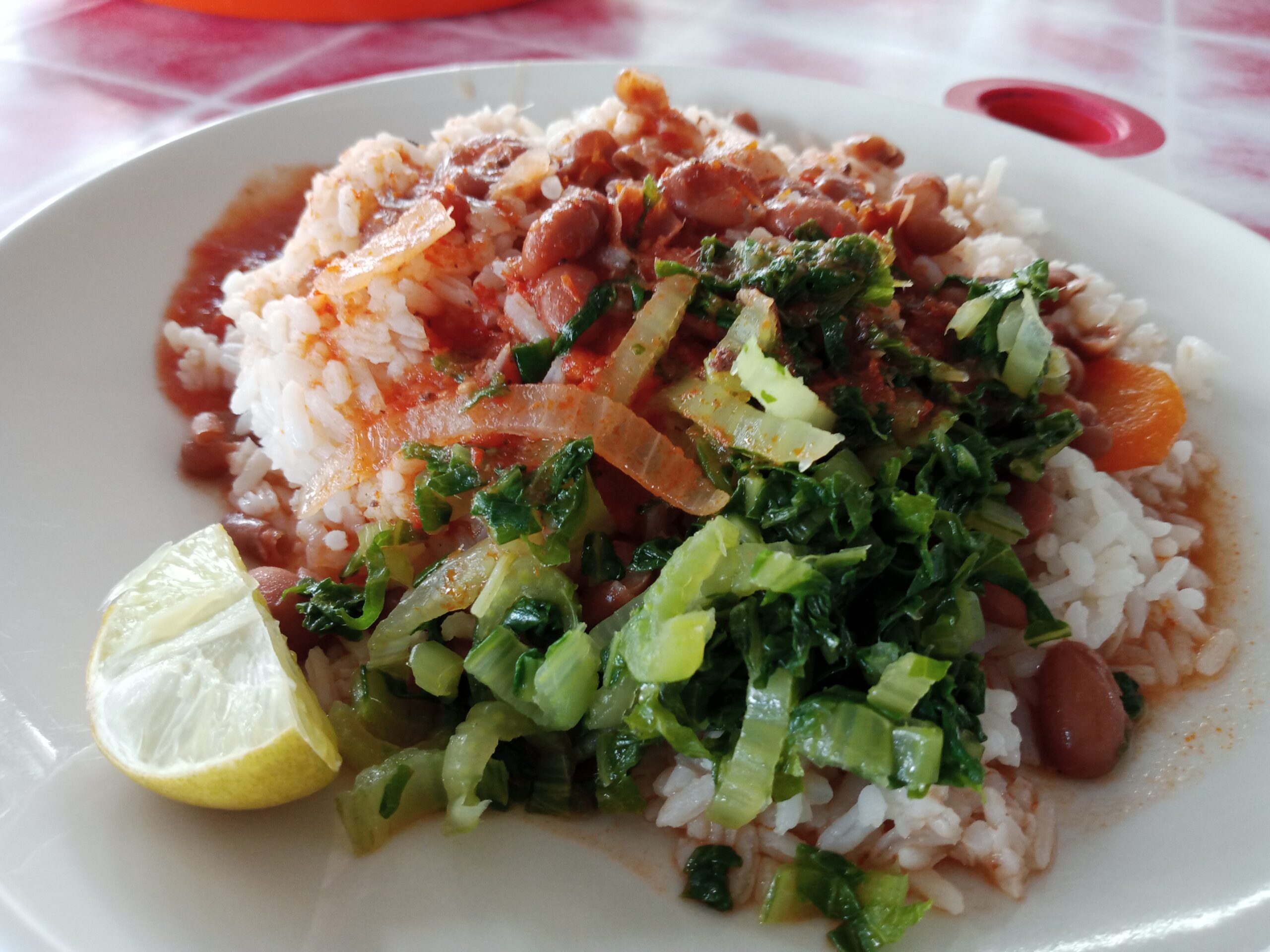 A plate containing white rice, beans, cooked green vegetables and a lime wedge.